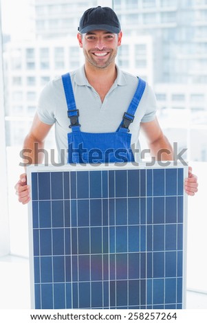 Portrait of smiling handyman holding solar panel in bright office