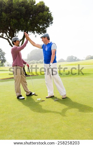 Golfing friends high fiving on the hole at the golf course