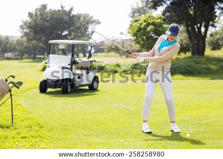 Female concentrating golfer teeing off on a sunny day at the golf course