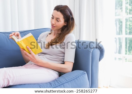 Casual woman reading book on couch at home in the living room