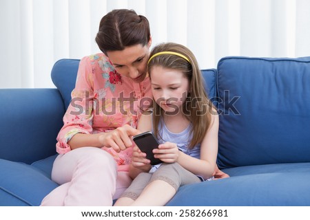 Mother and daughter using smartphone on couch at home in the living room