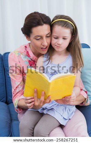 Mother and daughter reading book at home in the living room