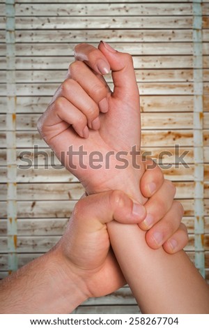 Male hand grabbing female wrist against wooden background in pale wood