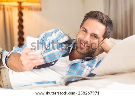 Handsome man relaxing on his bed with phone at home in bedroom