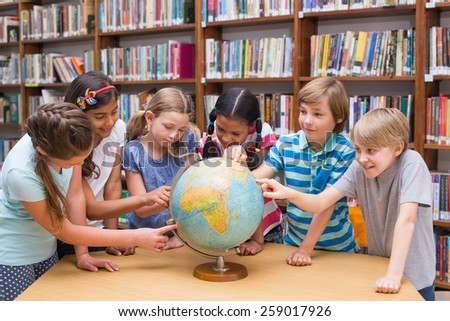 Cute pupils looking at globe in library at the elementary school