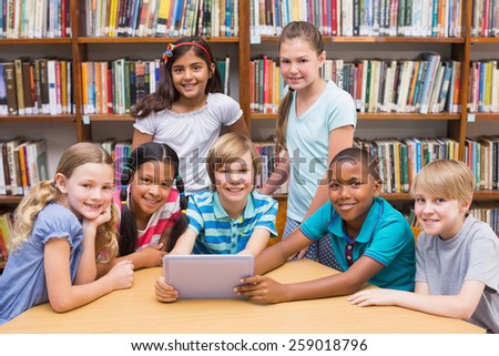 Cute pupils using tablet computer in library at the elementary school