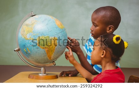Side view of little kids pointing at globe in classroom
