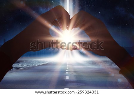 Woman making heart shape with hands against road leading out to the horizon with light beam