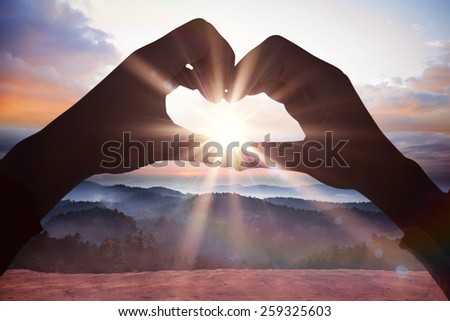 Woman making heart shape with hands against epic mountain scenery