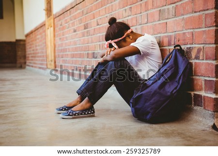 Full length of tensed girl sitting against brick wall in school corridor