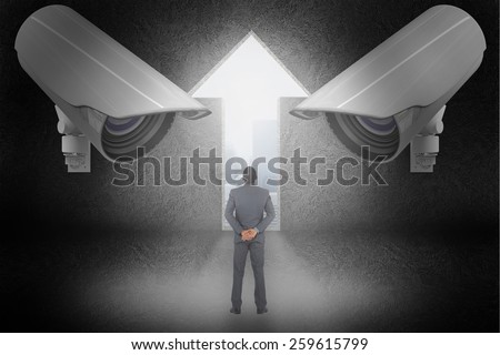 Young businessman standing with hands behind back against light bulb graphic on futuristic background