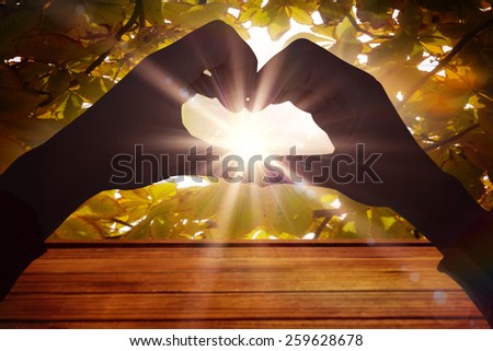 Woman making heart shape with hands against sun shining through leaves