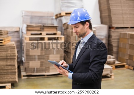 Warehouse manager wearing hard hat using tablet in a large warehouse