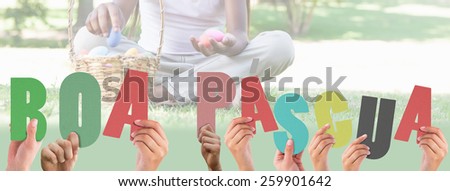 Hands holding up boa pasqua against little girl sitting on grass counting easter eggs smiling at camera