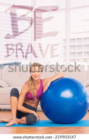 Slim blonde sitting beside exercise ball smiling at camera against be brave