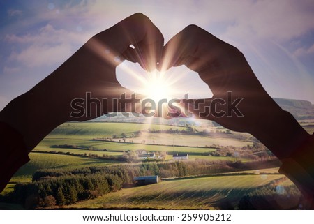 Woman making heart shape with hands against scenic landscape