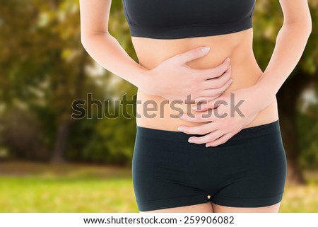 Mid section of a fit young woman with stomach pain against trees and meadow in the park