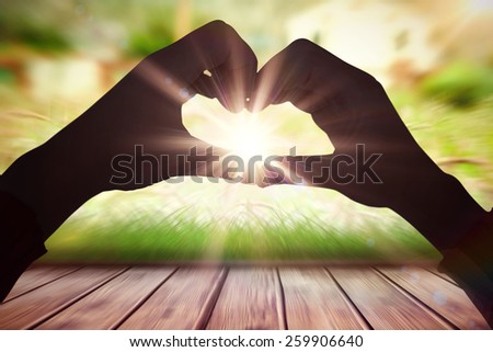 Woman making heart shape with hands against wooden planks against farm scene