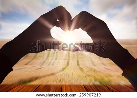 Woman making heart shape with hands against wooden planks overlooking corn field