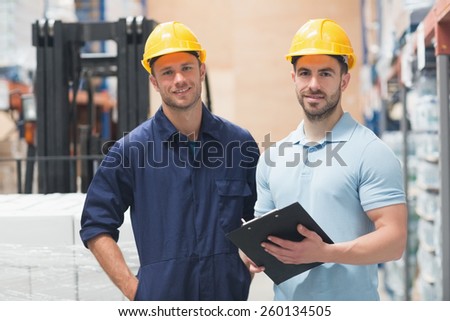 Smiling colleague posing with clipboard in warehouse