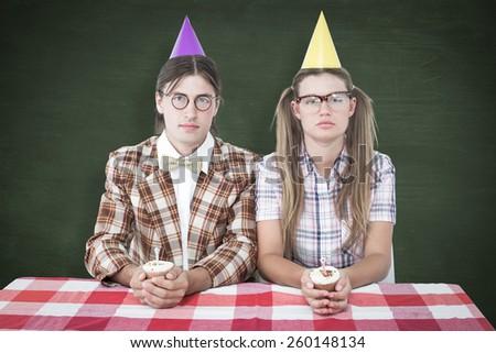 Unsmiling geeky hipsters celebrating birthday against green chalkboard
