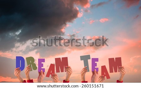 Hands holding up dream team against orange and blue sky with clouds
