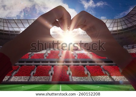 Woman making heart shape with hands against football stadium full of england fans