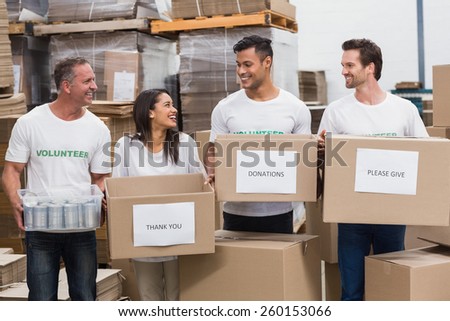 Happy team of volunteers holding donations boxes in a large warehouse