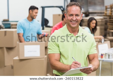 Smiling volunteer man taking notes holding clipboard in a large warehouse