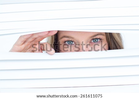 Woman peering through roller blind on white background