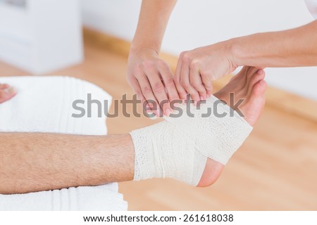 Doctor bandaging her patient ankle in medical office