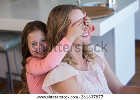Happy little girl covering her mother eyes at home