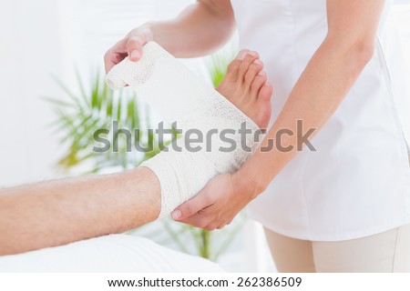 Doctor bandaging her patient ankle in medical office