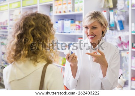 Pharmacist holding a bottle of drugs talking to customer in the pharmacy