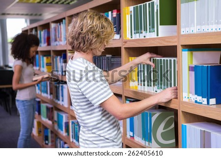Student picking a book from shelf in library at the university