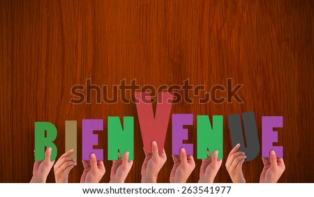 Hands holding up bienvenue against wooden oak table