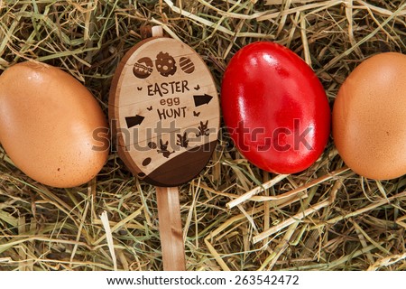Easter egg hunt sign against red egg on straw with plain ones