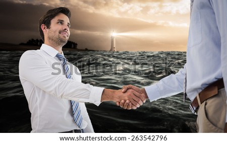 Young businessmen shaking hands in office against stormy sea with lighthouse