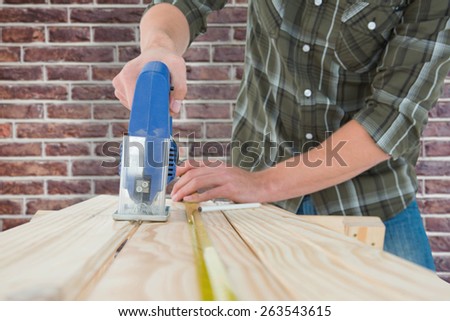 Carpenter cutting wooden plank with electric saw against red brick wall