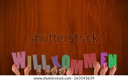 Hands holding up wilkommen against wooden oak table