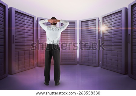 Businessman standing back to the camera with hands on head against server room with towers