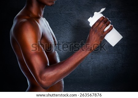 Mid section of a sporty young man holding protein drink against black background