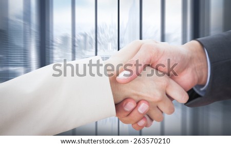 Close up on partners shaking hands against room with large window looking on city