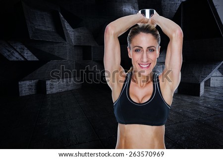 Female happy bodybuilder working out with large dumbbell behind head against dark room