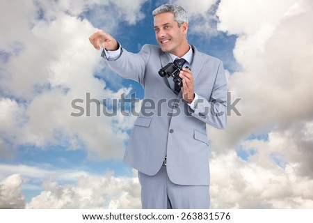 Businessman holding binoculars and pointing out something against blue sky with white clouds