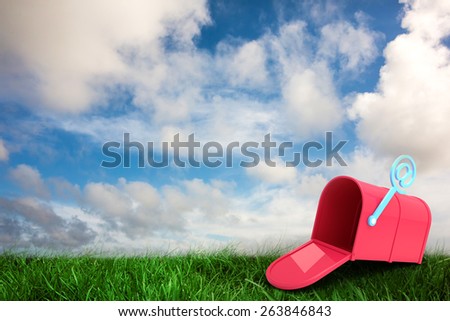 Red email post box against green grass under blue sky