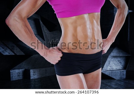 Female bodybuilder posing with hands on hips mid section against dark room