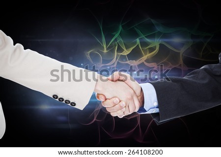 Smiling business people shaking hands while looking at the camera against black background with spark