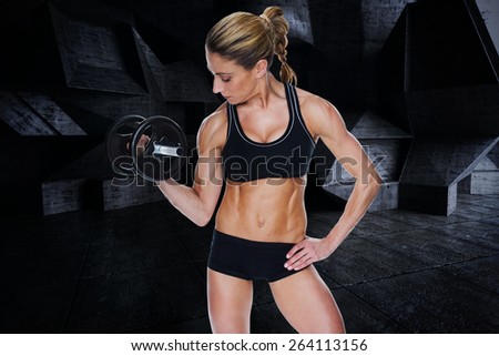 Female bodybuilder holding large black dumbbell with arm up looking at bicep against dark room