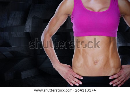 Female bodybuilder posing with hands on hips mid section against dark room